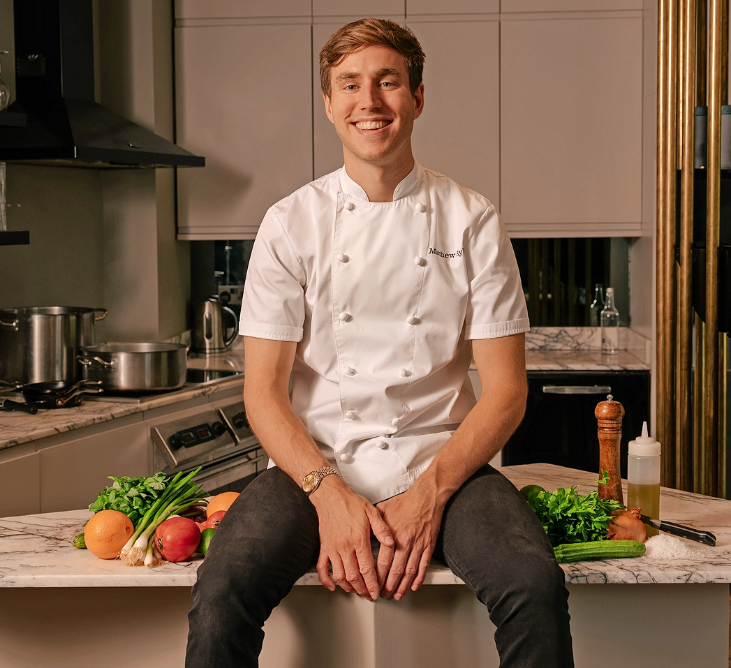 Matthew Ryle sitting on a kitchen counter with fresh produce.