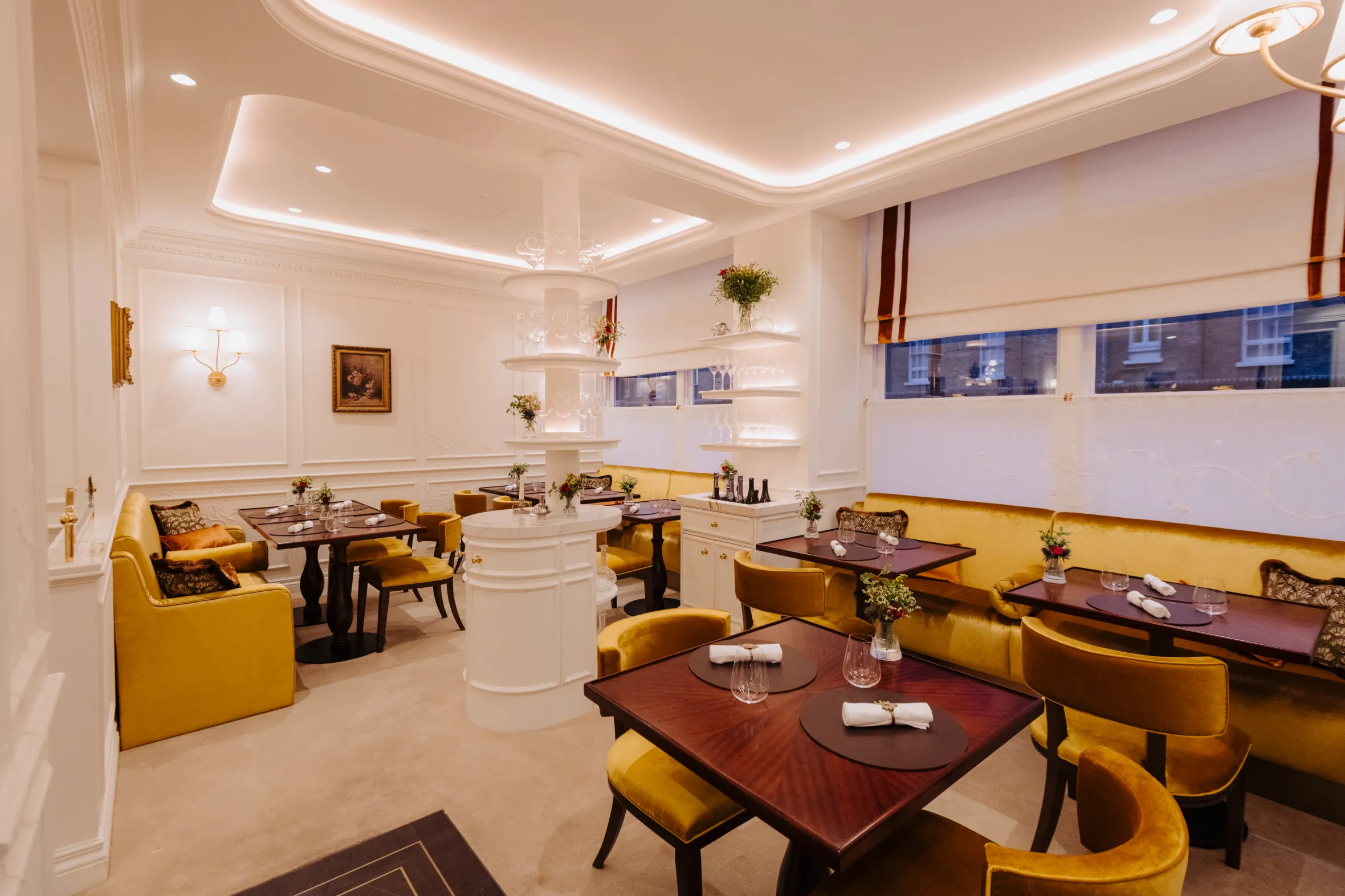 The dining room of Core restaurant with mustard yellow chairs and booths, wooden tables, and white walls with decorative molding.