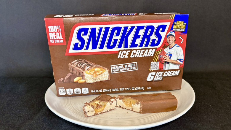 Snickers ice cream bar cut open on plate with box in background