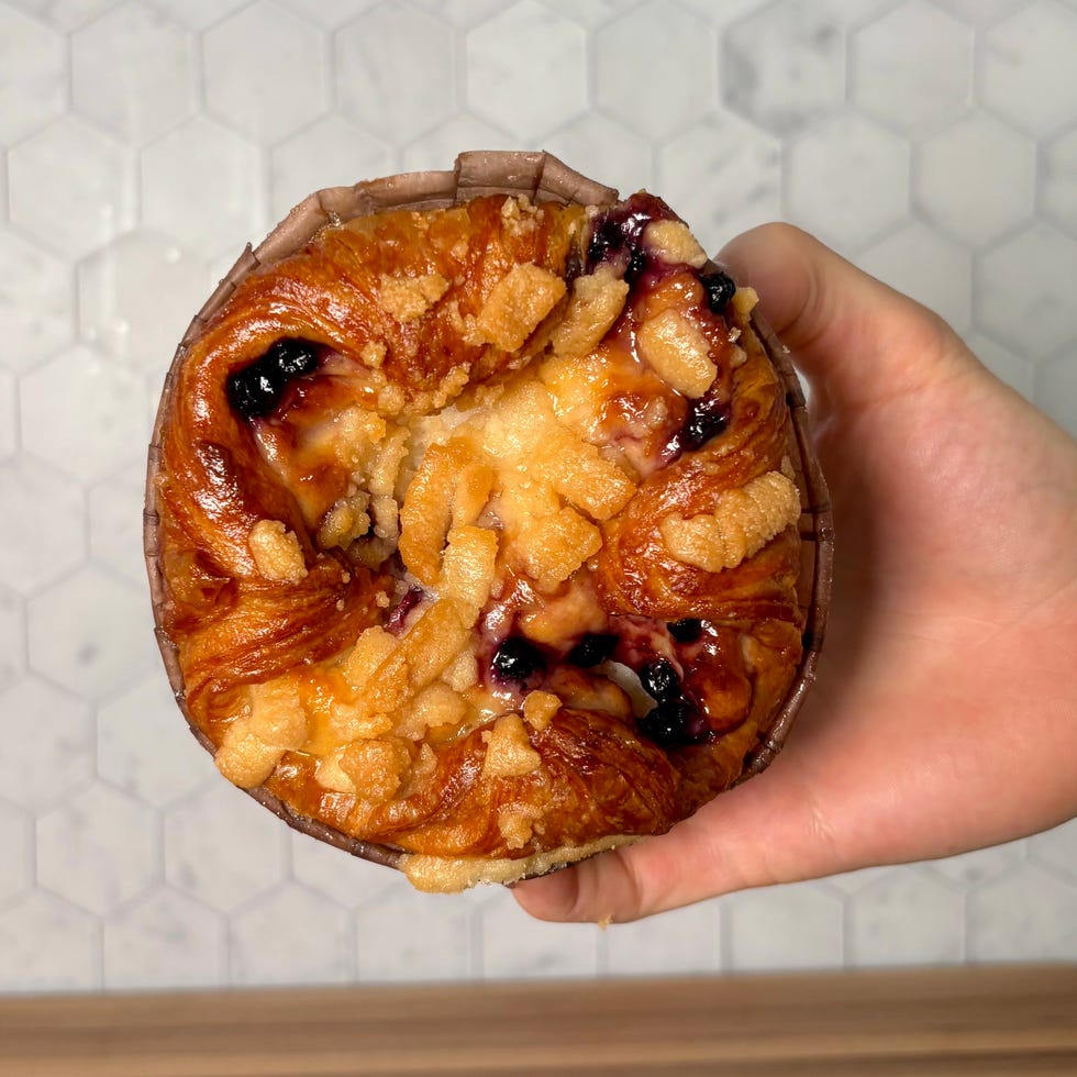 A sweet pastry held in a hand, featuring a glazed top with berries and crumbles.