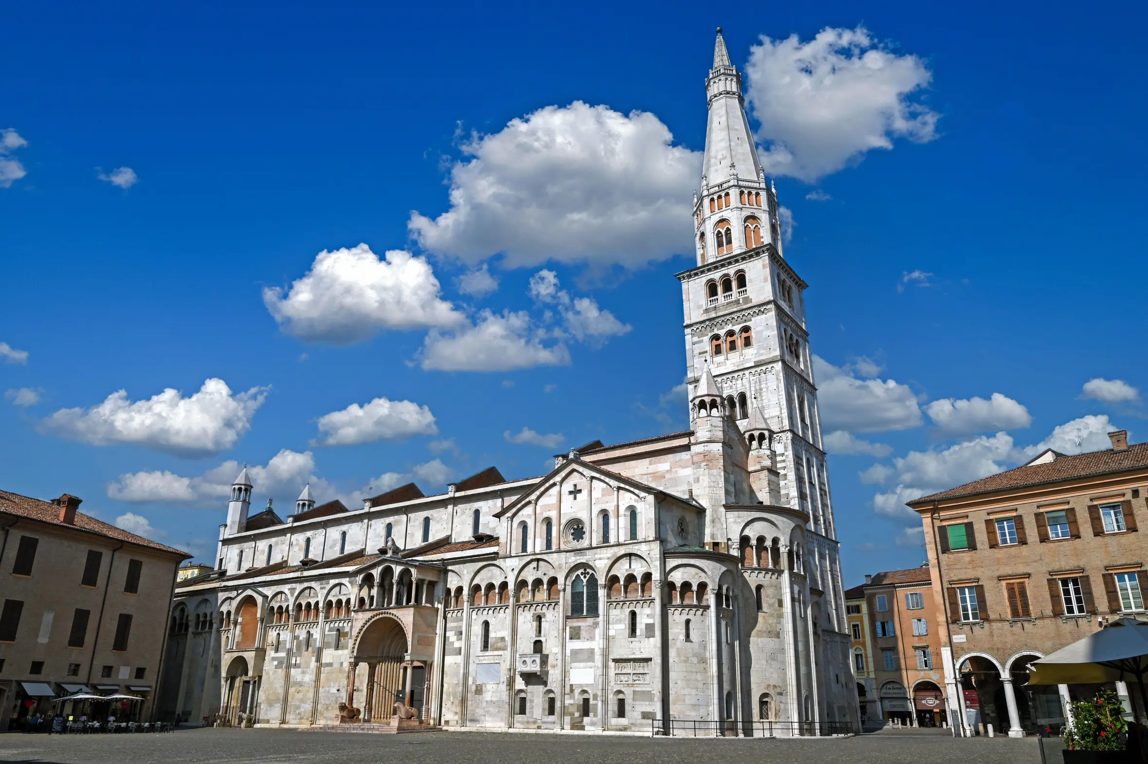 Modena Cathedral and Ghirlandina bell tower on a sunny day with blue sky and white clouds.