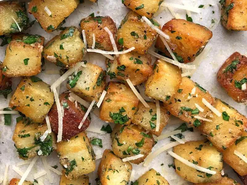 Crispy golden-brown potato cubes garnished with parsley and grated cheese on parchment paper.