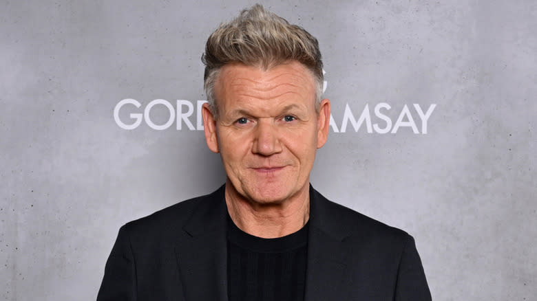 Close-up headshot of Gordon Ramsay in a black suit against gray sign