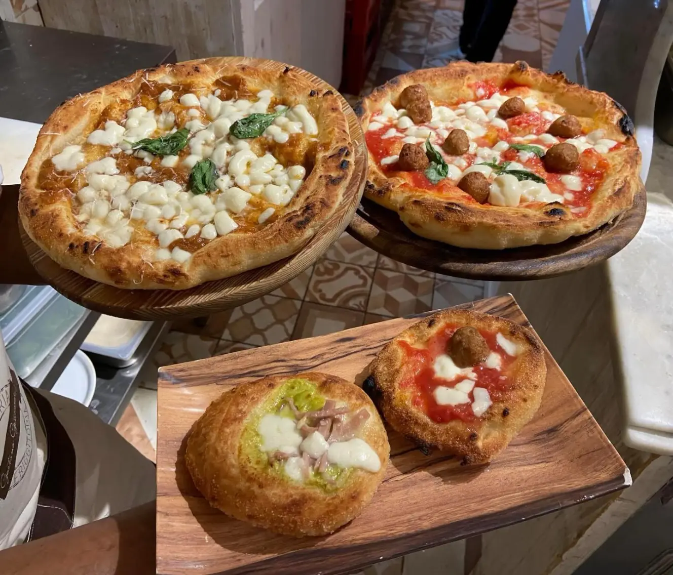 Two pizzas with meatballs and two small pizzas with various toppings served on wooden boards.