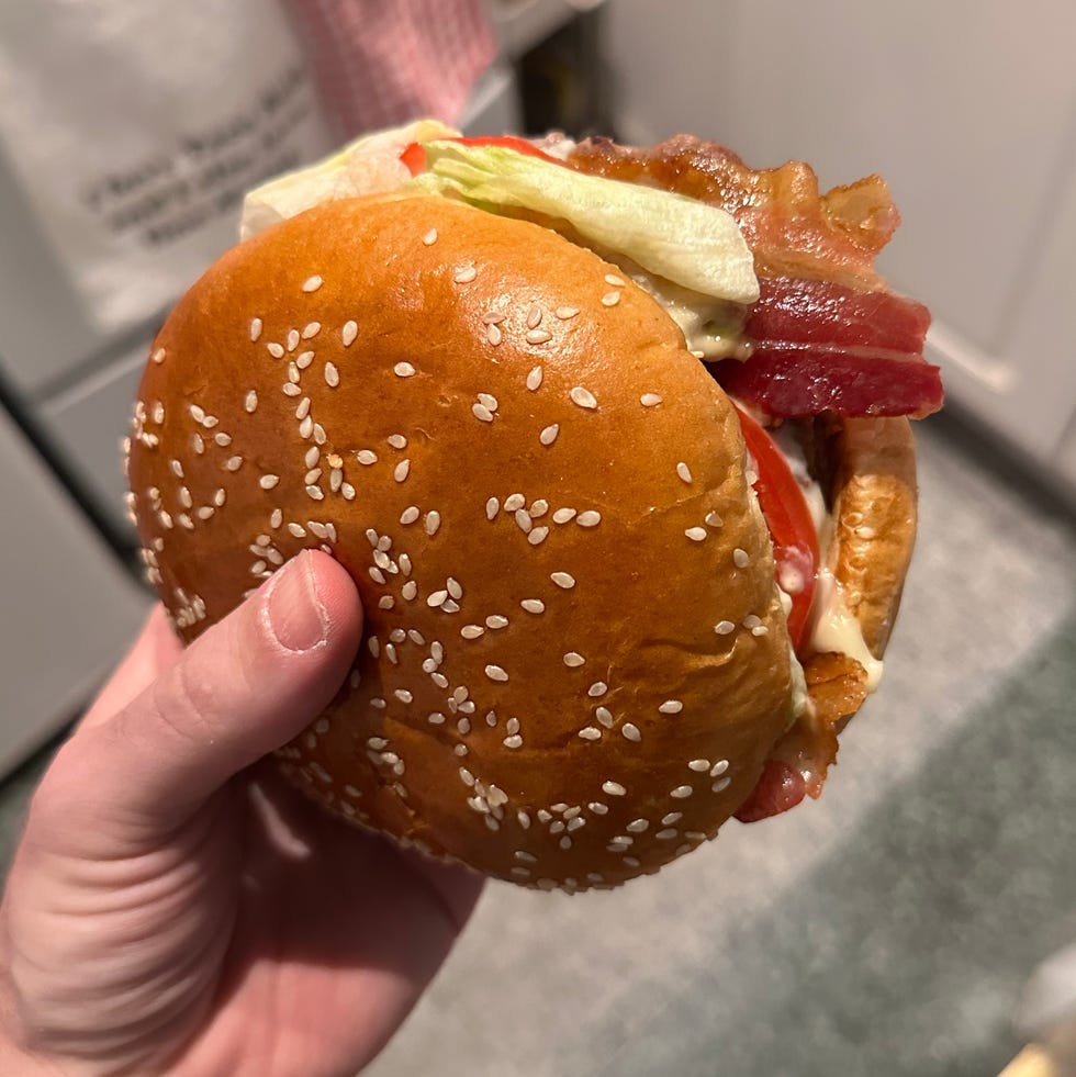 Hand holding a burger with bacon, lettuce, and tomato.
