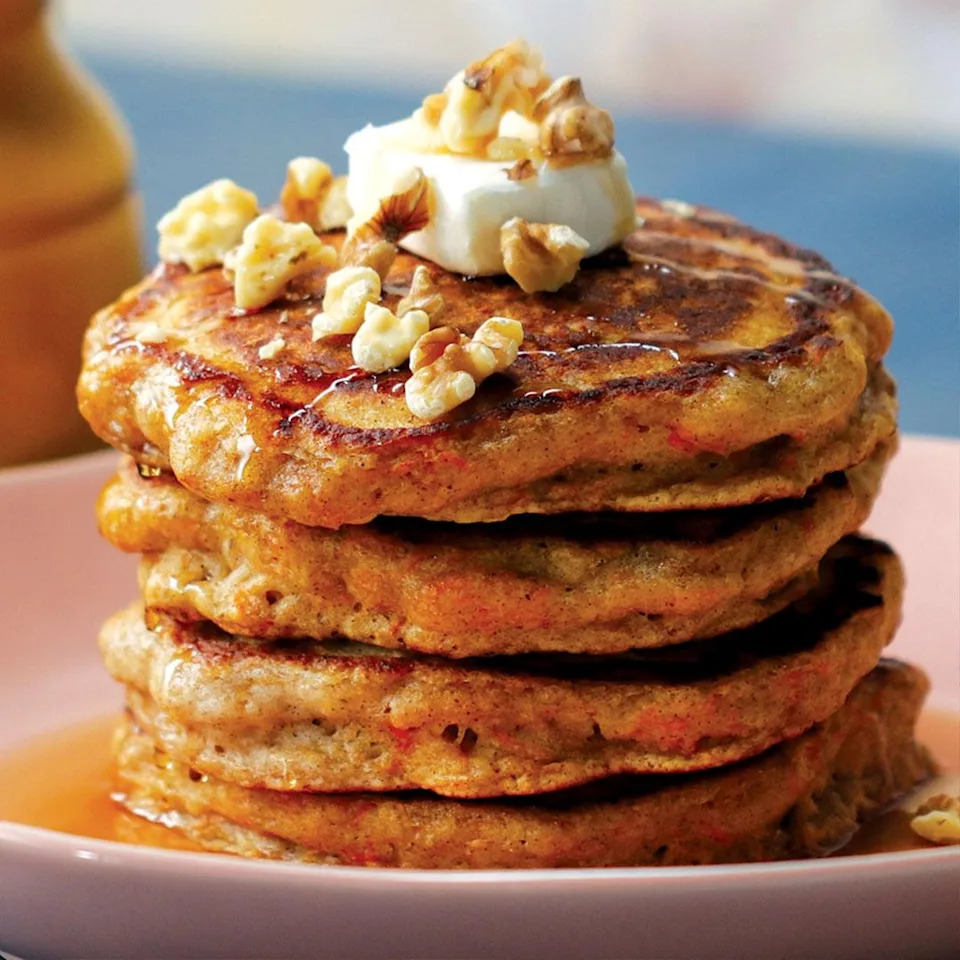 Stack of pancakes topped with walnuts, butter, and syrup on a plate