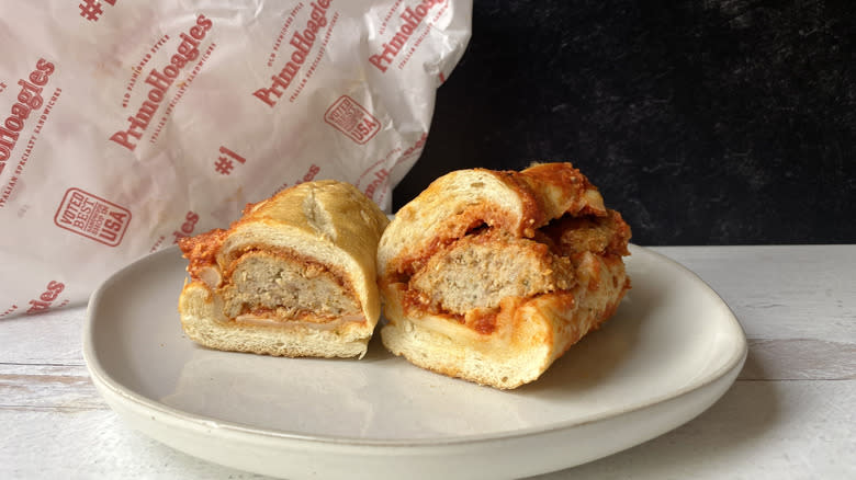 A Primo's meatball sub cut in half on a small plate in front of the to-go packaging