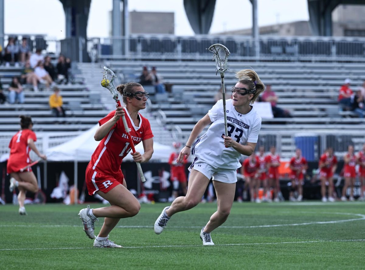 Two lacrosse players run across a field. 