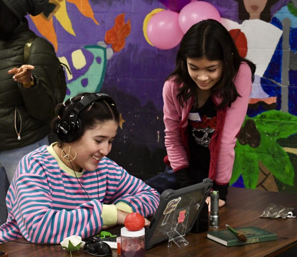 Two girls laugh while working on a laptop.