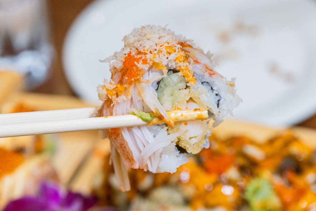 A piece of sushi with rice, a green filling and an orange topping.