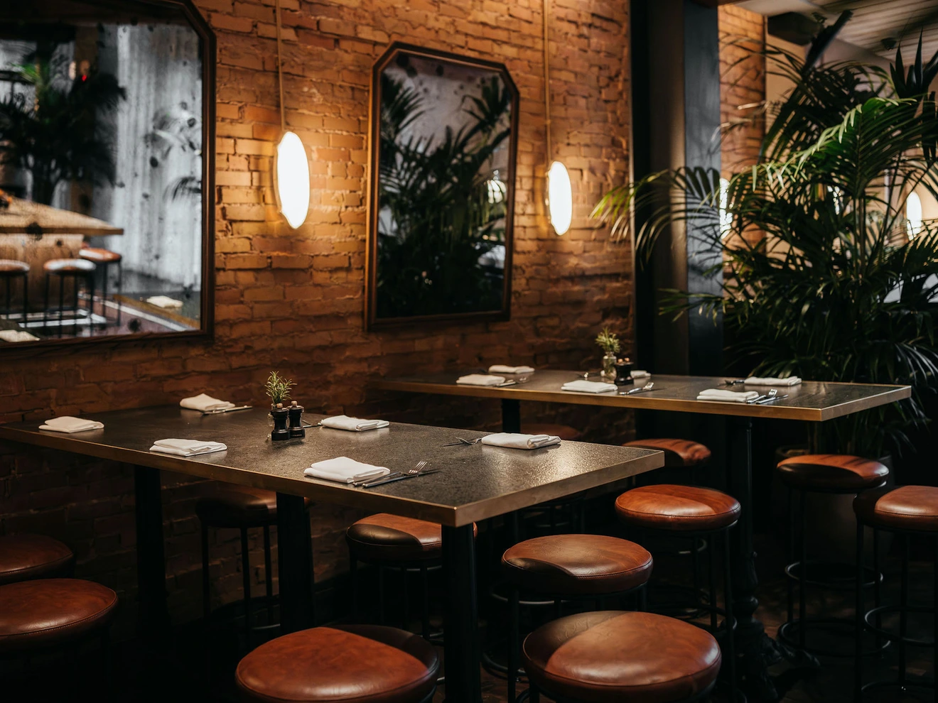 Cozy restaurant interior with brick walls, leather stools, mirrors, and dim warm lighting.