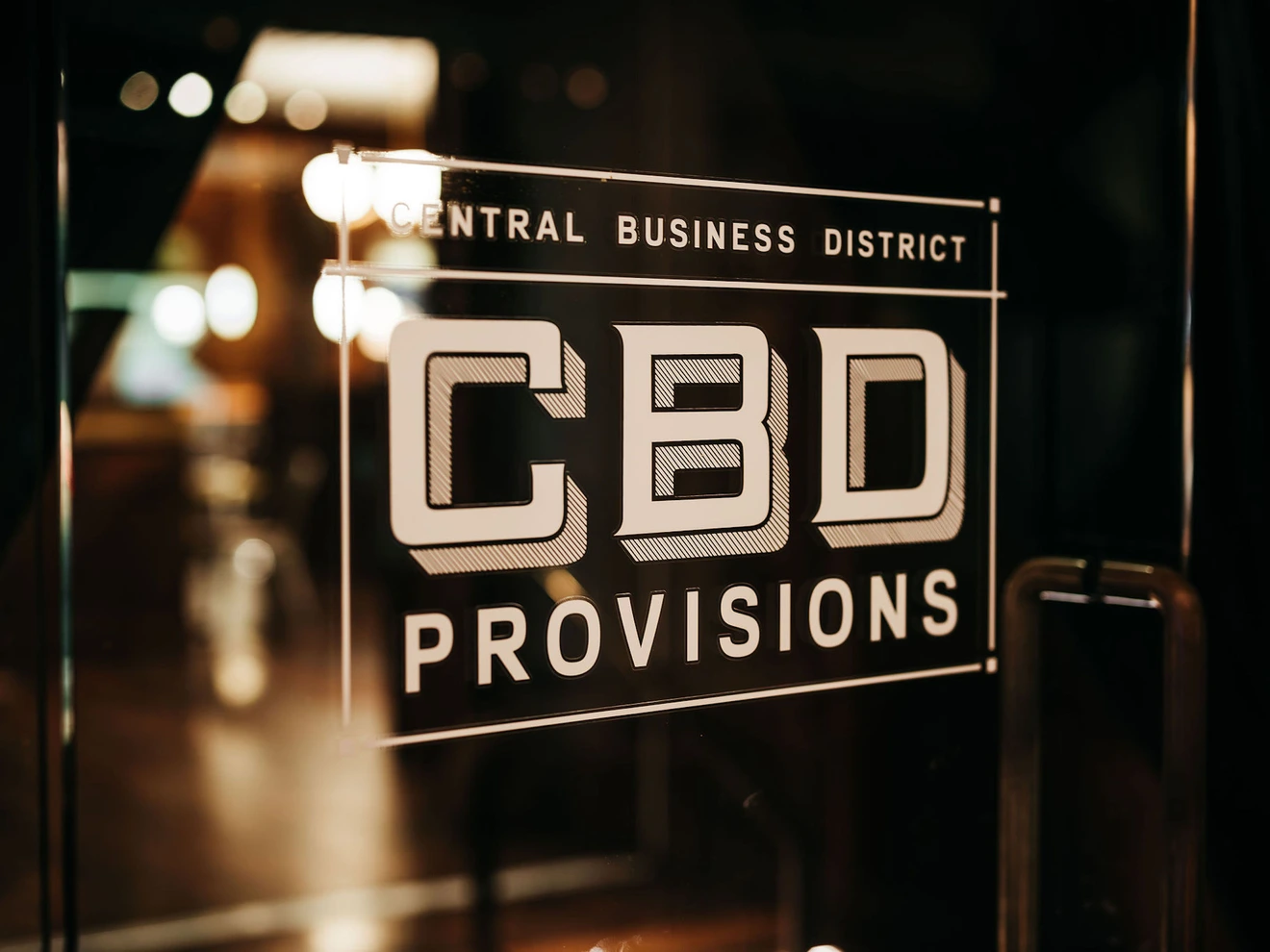 Glass door with Central Business District CBD Provisions sign in a dimly lit setting.