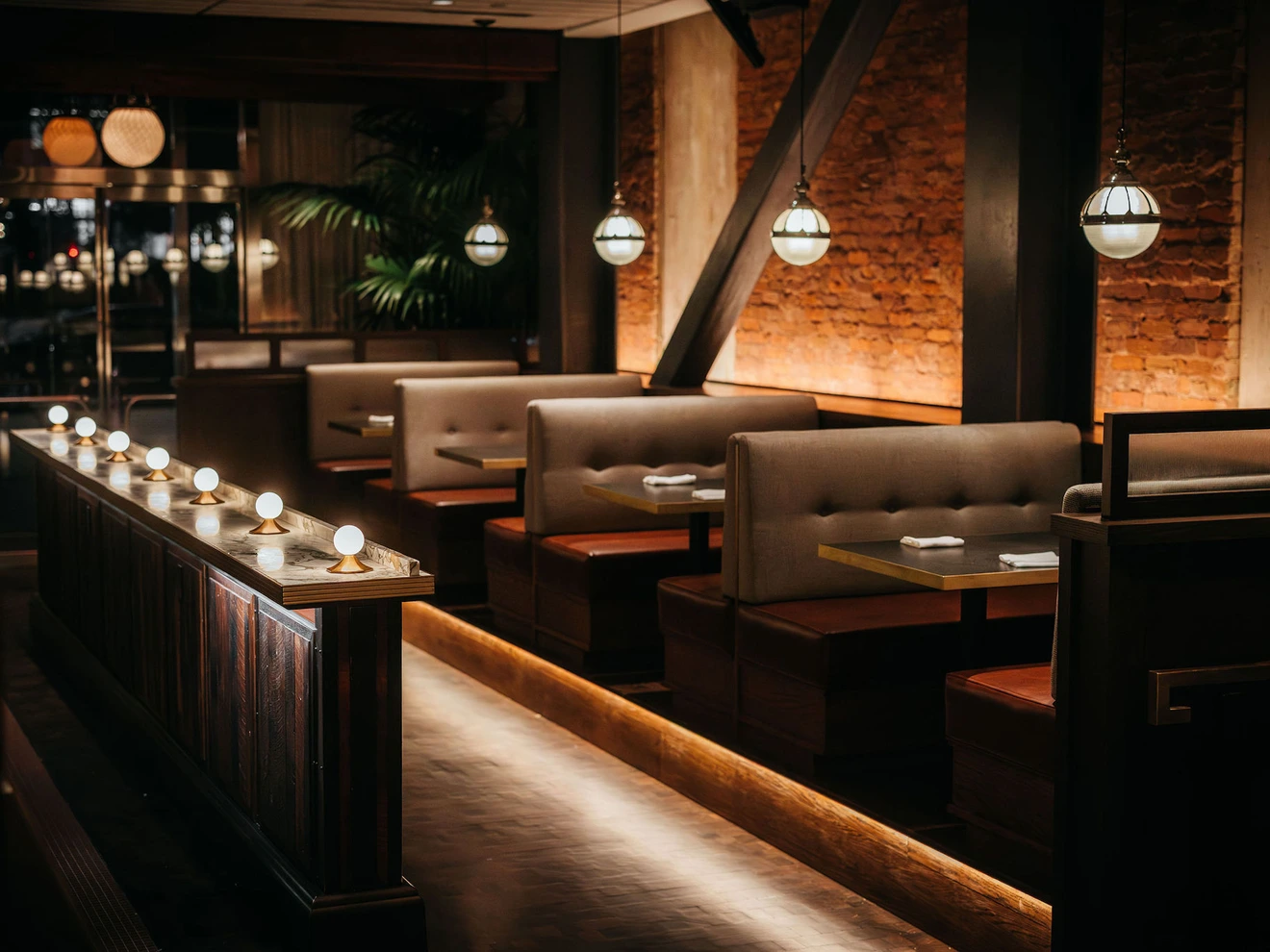 Interior of a modern, dimly lit restaurant with booth seating and warm ambient lighting.