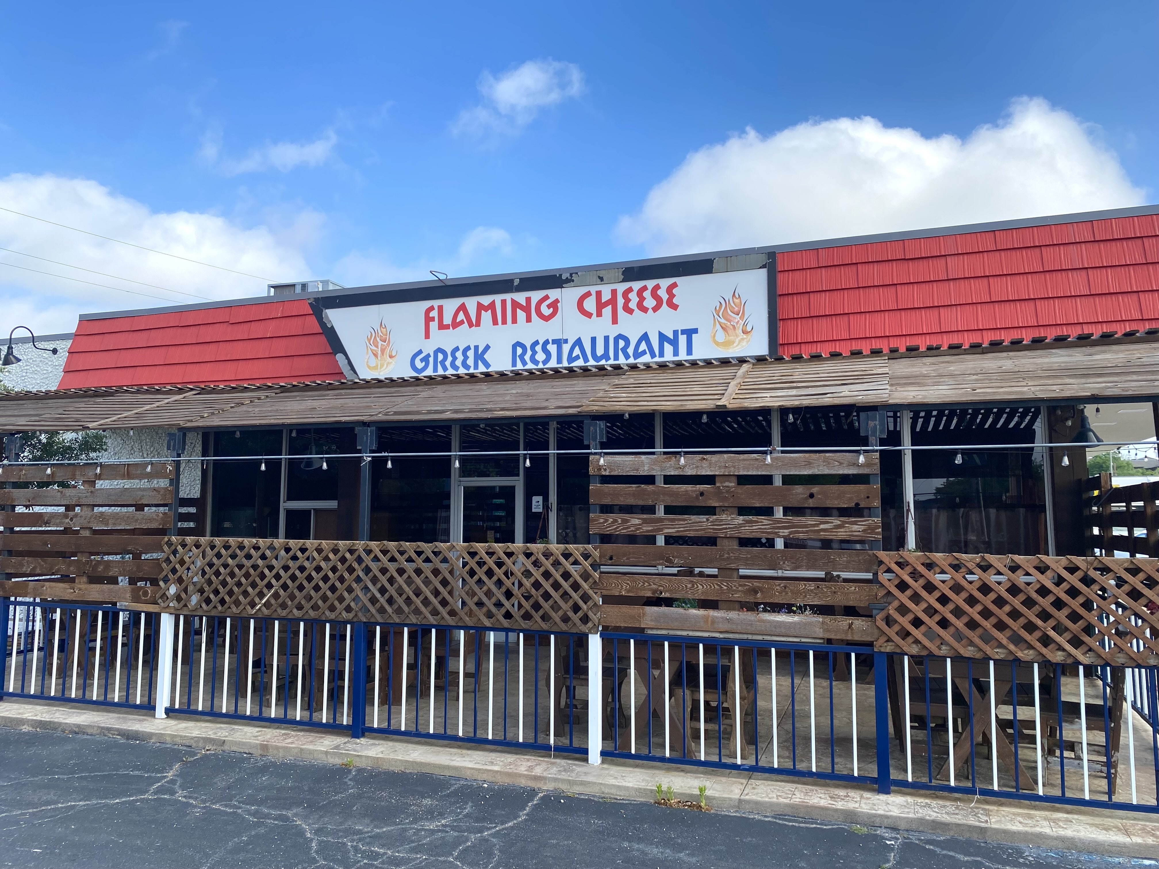 The exterior of Flaming Cheese, a Greek restaurant. There's a red awning and an enclosed patio.
