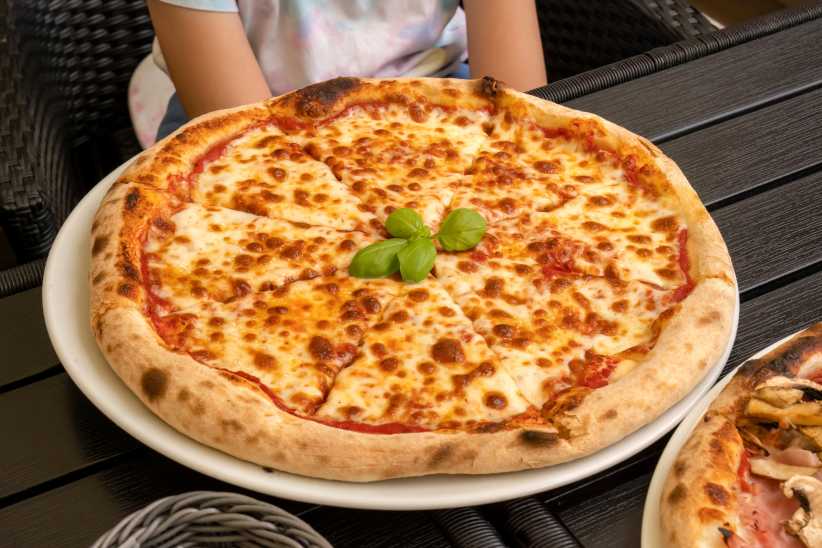 Classic Margherita pizza without additional toppings on the table served in a restaurant, pizzeria, closeup shot thick layer of melted cheese, high angle, one person sitting at the table, basil leaves, The Best Pizza Spots in Westchester Right Now,