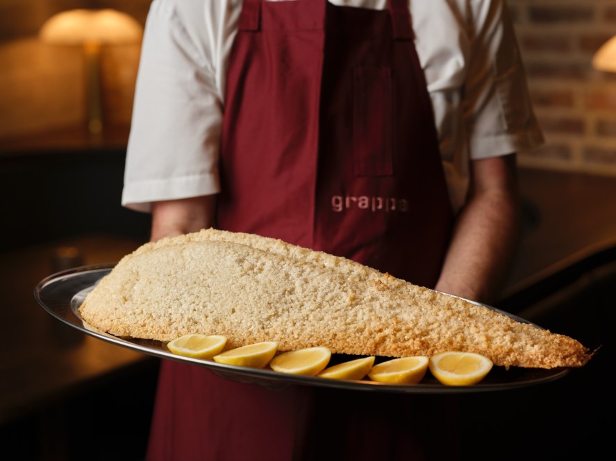 Grappa waiter wearing red apron carries a salt-baked snapper