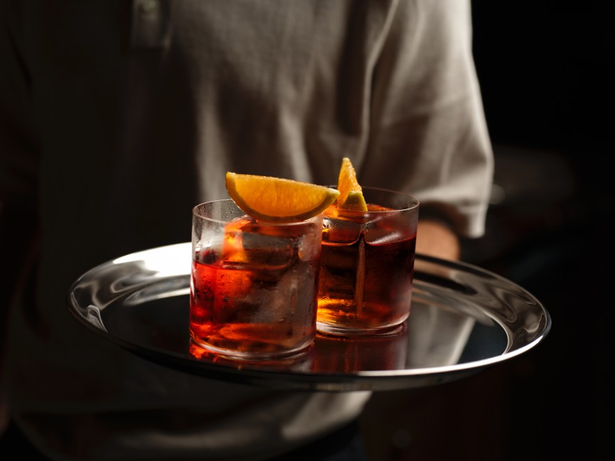 A waiter holds a silver tray with two negronis