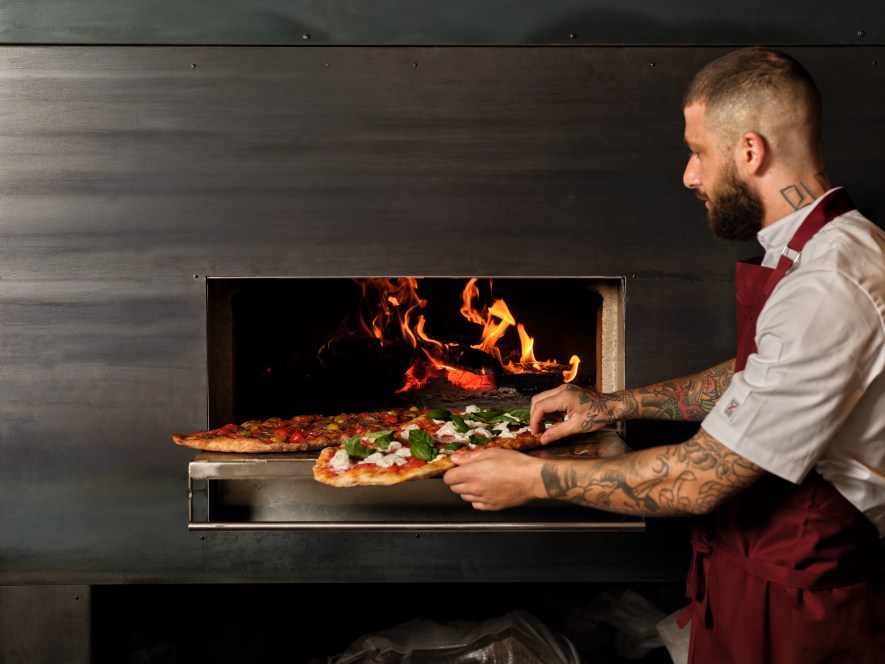 Alessandro Penna puts pizzas in the oven at Grappa