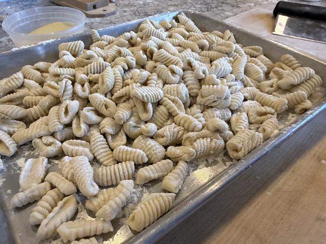 A tray of gnocchi, made using a rigagnocchi (a small wooden ridged board), which sits in the top left of the photo, next to a container of semolina.