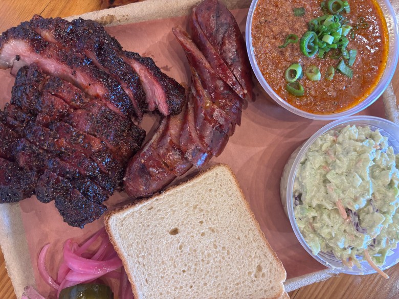 Smoked brisket and ribs served on butcher paper with coleslaw, BBQ sauce, white bread, and pickled onions