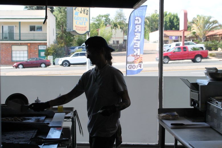 Silhouette of a woman leaning over a grill with a bright street scene outside