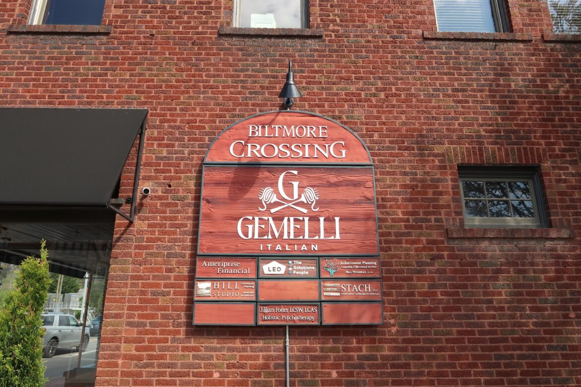 Brick building façade with an arched red sign reading 'Biltmore Crossing Gemelli Italian' and smaller tenant plaques below.
