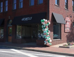Brick storefront with a dark awning reading 'GEMELLI ITALIAN'; balloon arch in teal, white, mint, and bronze beside the entrance