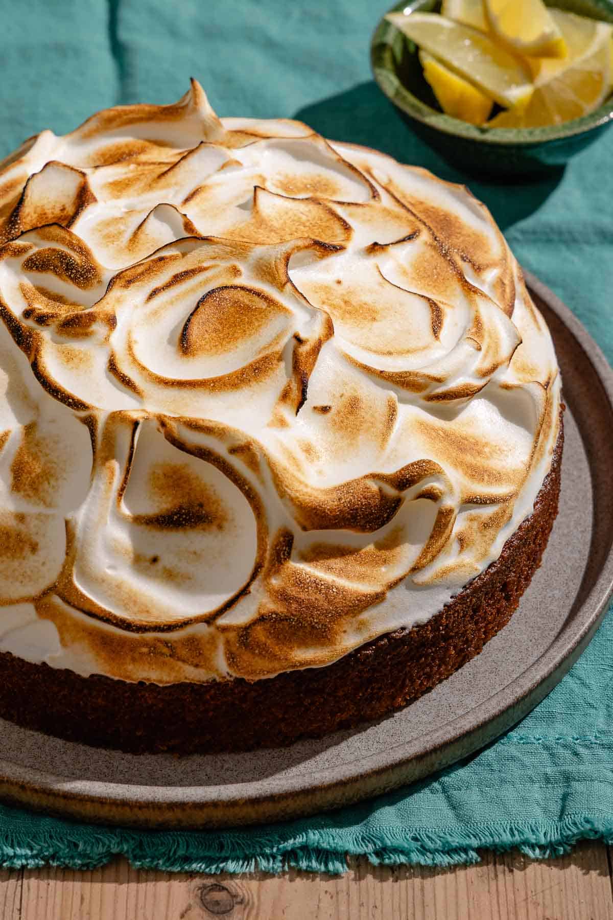 The entire limoncello cake on a platter next to a bowl of lemon wedges.