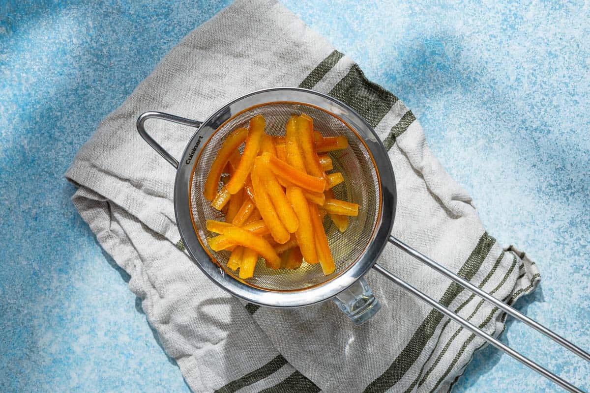 candied orange peels being strained into a heatproof bowl.