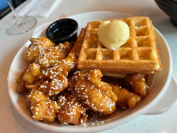 Sesame chicken bits next to two square waffles with a scoop of butter on top