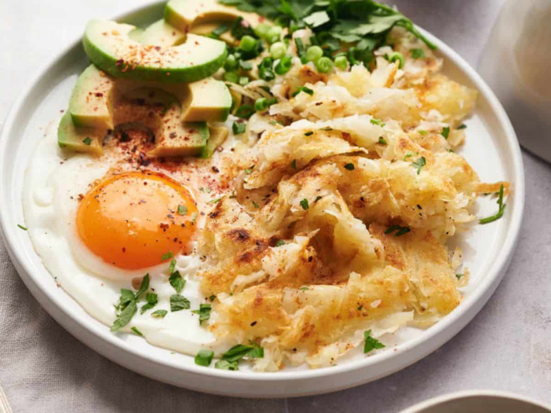 Hash Browns on a white plate with an egg and avocado.