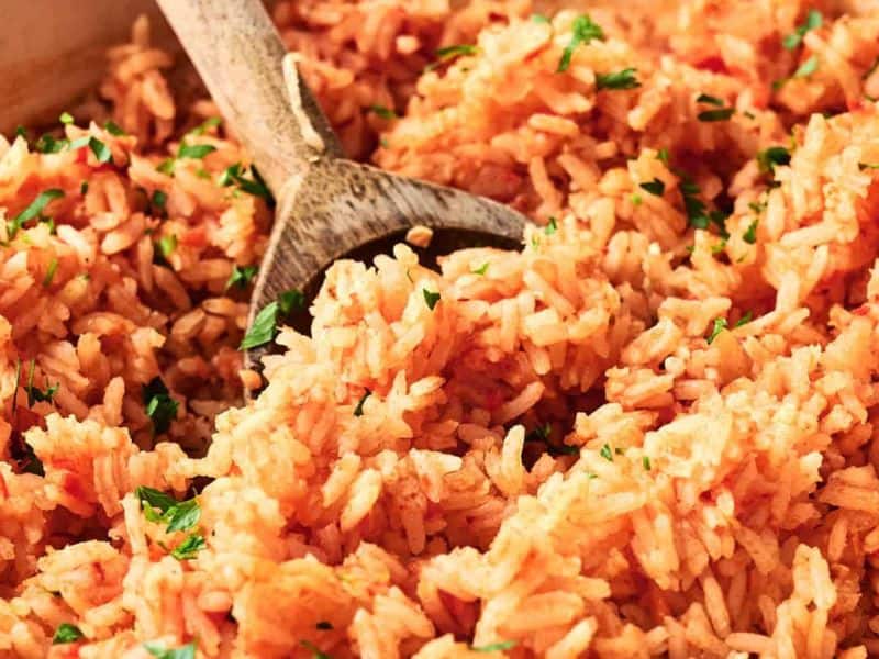 A close-up of cooked Mexican rice with a wooden spoon, garnished with chopped parsley.