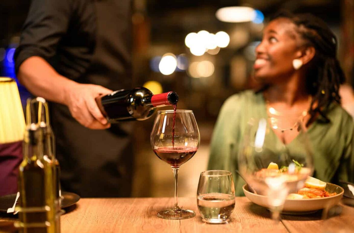Woman enjoying wine and food at African restaurant with waiter pouring red wine.