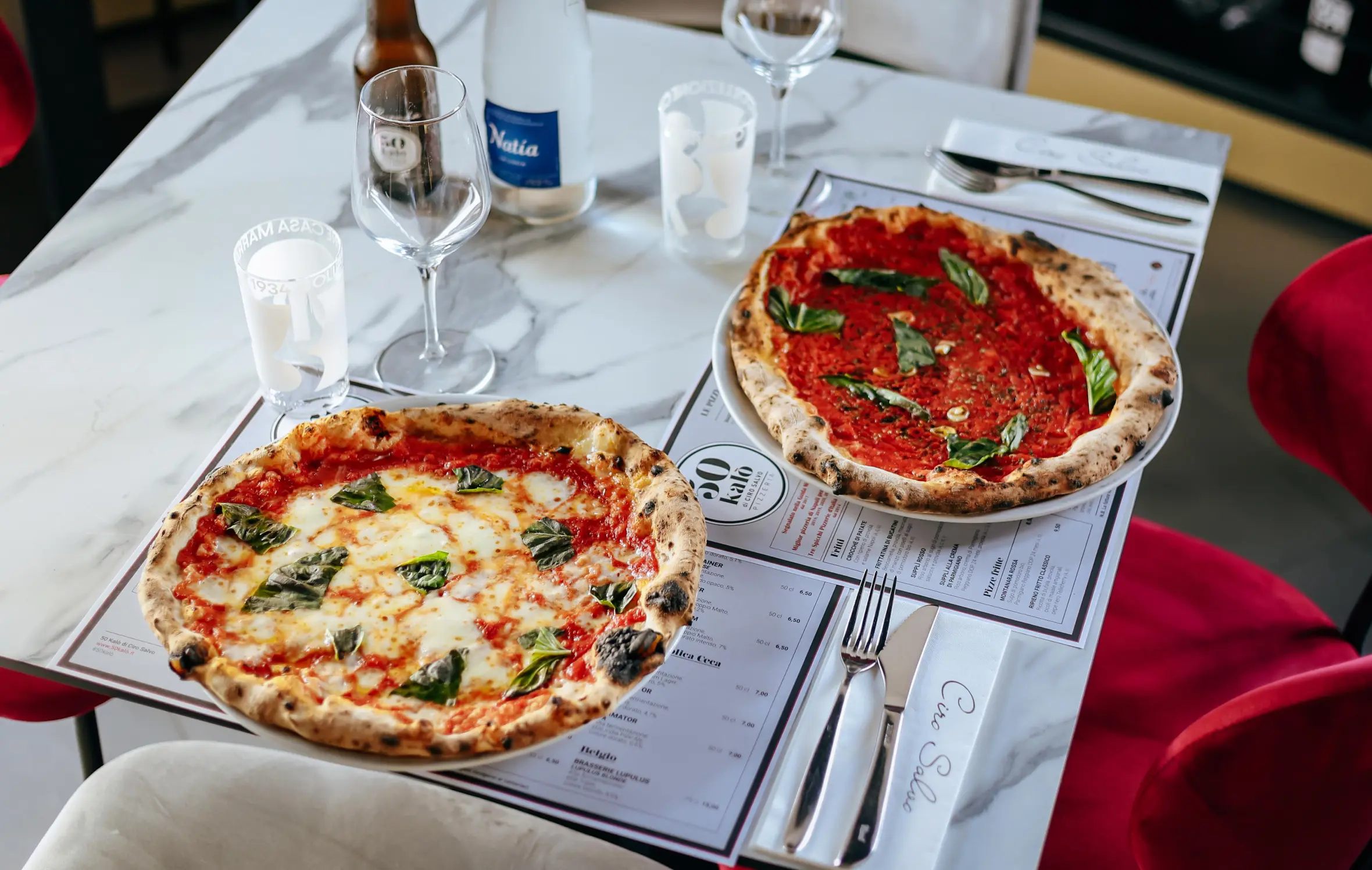 Two pizzas on a table, one Margherita and one marinara.