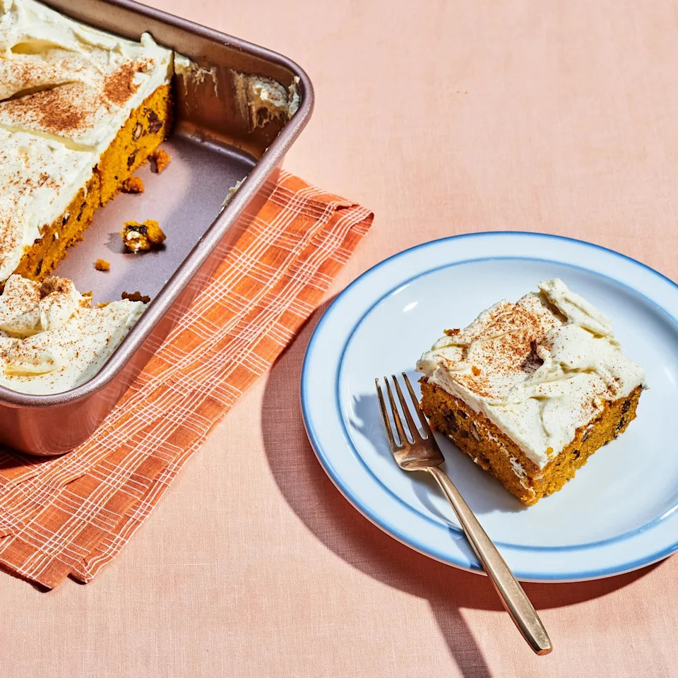 Slice of frosted cake on a plate with a fork, next to a baking dish with more cake