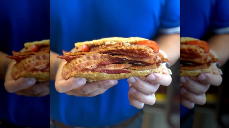 Man holding a BLT sub loaded with strips of bacon