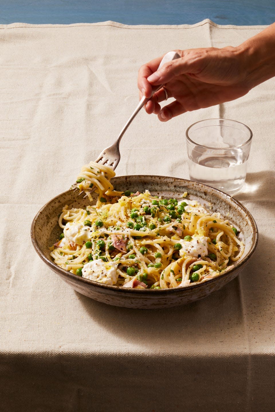 hand twirling pasta in bowl on dining table