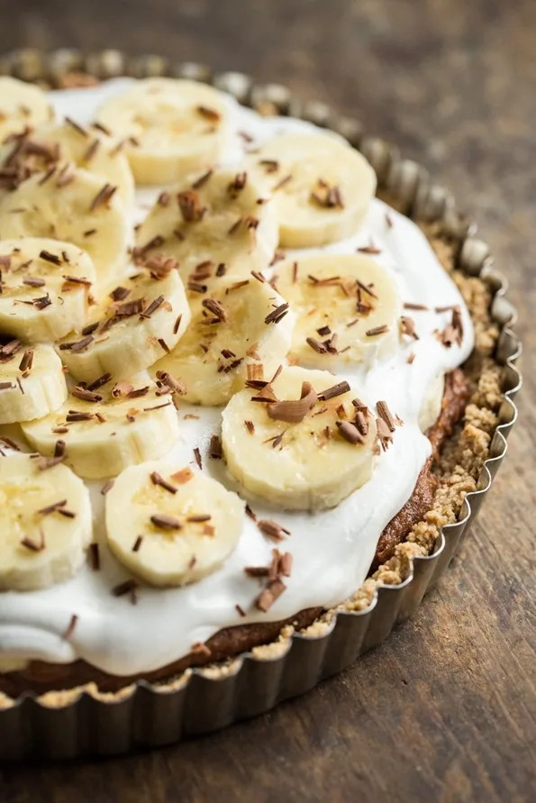 Banana cream pie topped with sliced bananas and chocolate shavings in a fluted metal pie dish