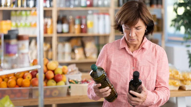 person in pink shirt comparing olive oils in supermarket
