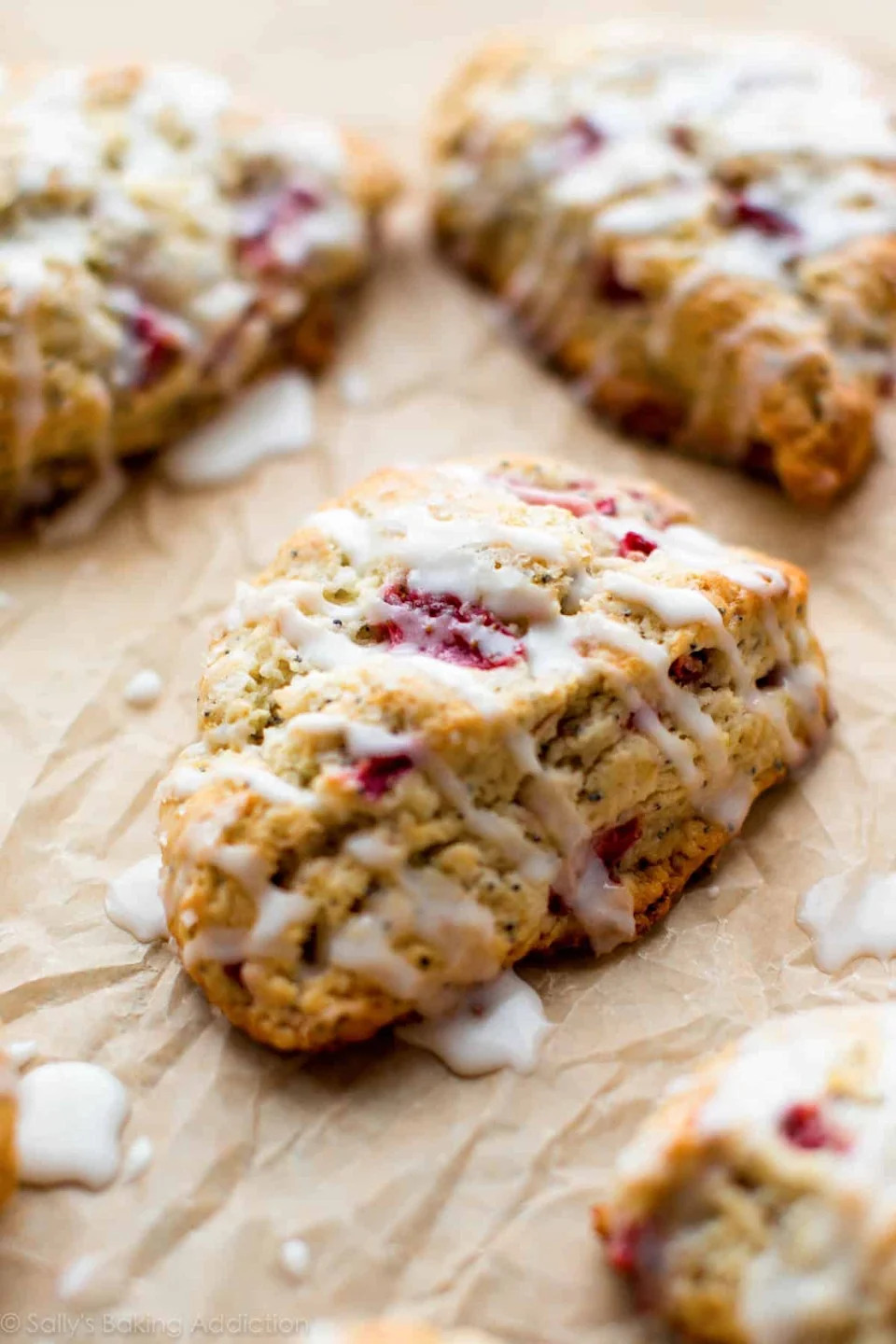 Scones with a drizzle of icing on parchment paper, featuring visible bits of fruit