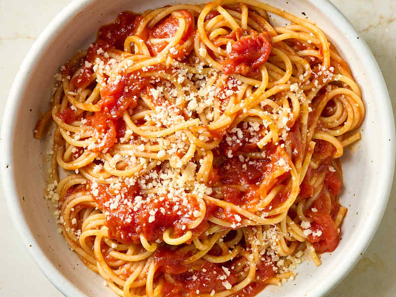 Spaghetti topped with marinara sauce and grated cheese in a white bowl.