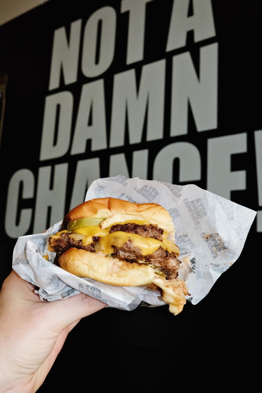 A hand holds a double cheeseburger against a black wall that says "NOT A DAMN CHANCE!"