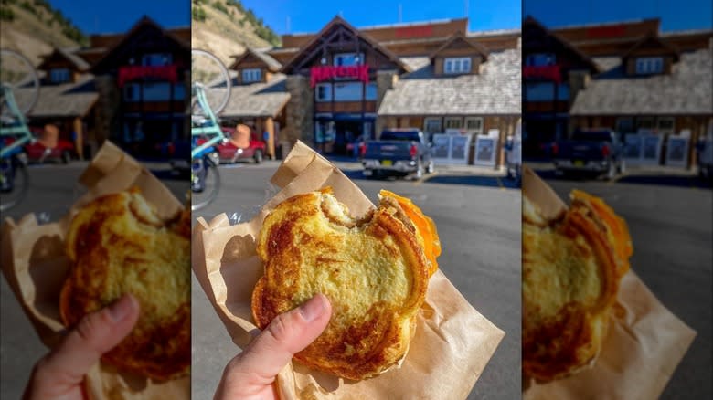 Hand holding a french toast breakfast sandwich with a Maverik convenience store in the background
