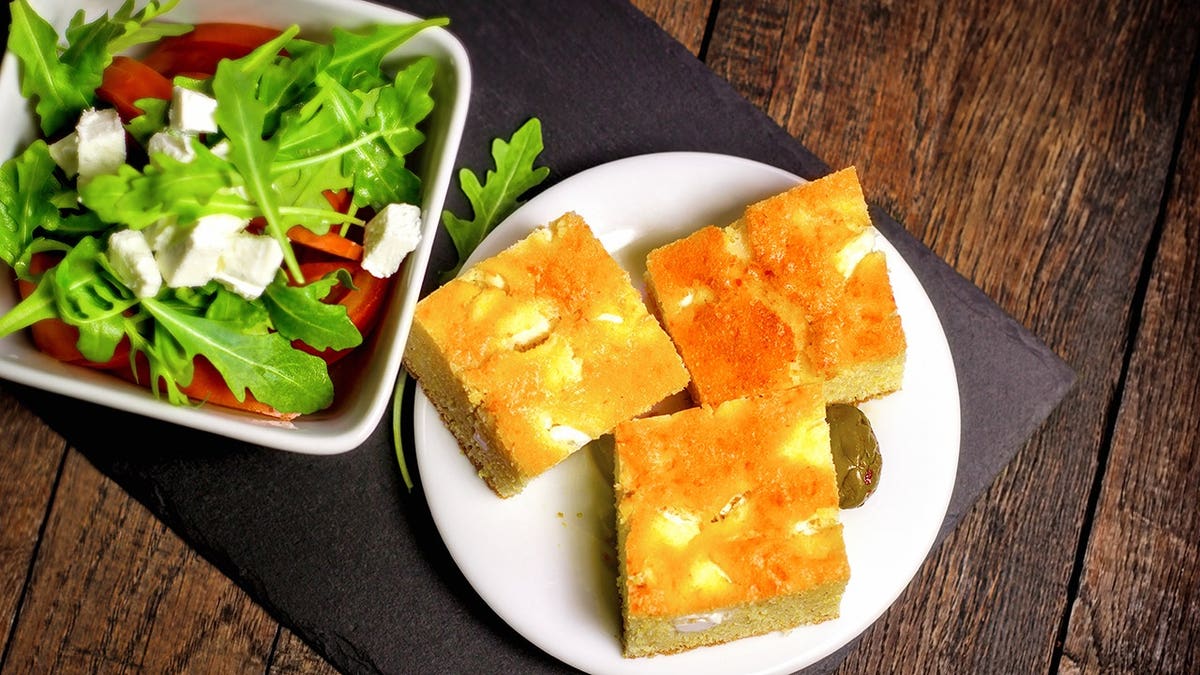 Cornbread and salad served on a plate on a rustic wooden table.