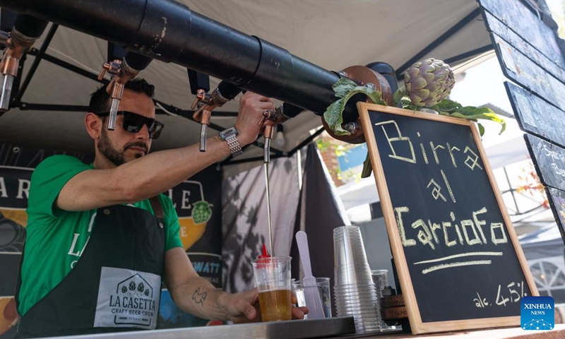A vendor fills a cup with artichoke beer from a tap during a Roman artichoke festival in Ladispoli, Italy, April 10, 2026. The annual festival celebrating the harvest of the Roman artichoke kicked off on Friday. (Xinhua/Li Jing)