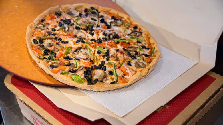 Veggie pizza being slid into takeout box
