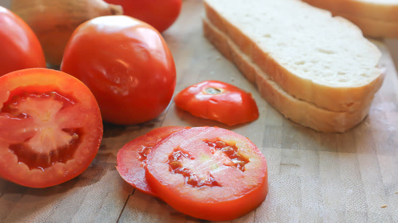 Slices of white bread next to whole and sliced tomatoes