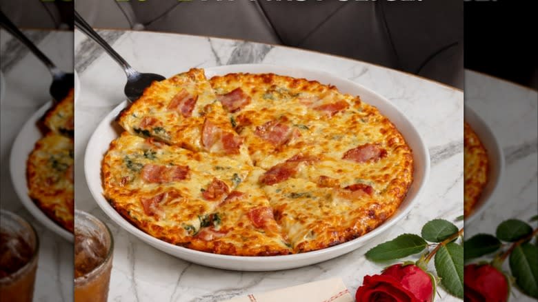 Spinach and bacon pizza from Olive Garden on white dish with serving knife next to red rose