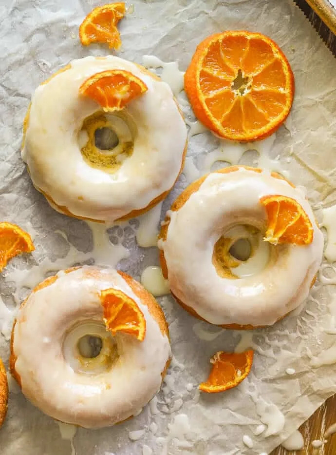 Three glazed donuts topped with orange slices on parchment paper