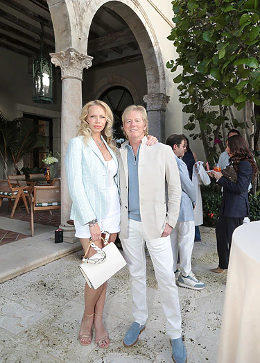 A couple posing at an elegant outdoor event with archways and greenery in the background.